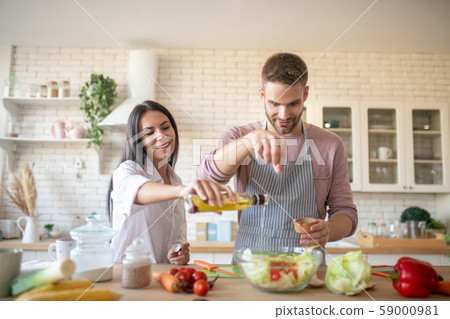 Husband adding spices to salad while cooking with wife Husband adding spices to salad while cooking with wife 59000981
