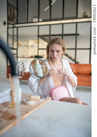 Blonde woman holding pink cosmetics bag and doing makeup 59002621