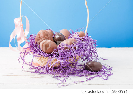 Photo of chicken , chocolate eggs, purple decorative paper in basket 59005541