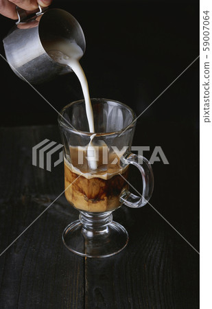Hand pouring milk in cold brew coffee on black wooden table. 59007064