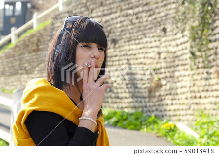 young brunette woman smoking cigarette outside young brunette woman smoking cigarette outside 59013418