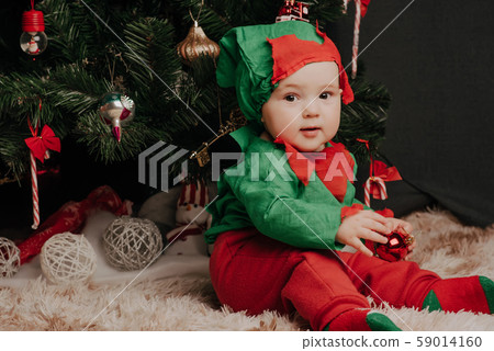 little boy in elf costume sits under a Christmas tree with balls little boy in elf costume sits under a Christmas tree with balls 59014160