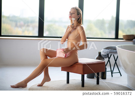 Slim blonde woman sitting in bathroom and cleaning her skin 59016372