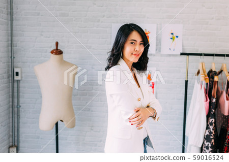 Confident Asian young female dressmaker having arms crossed with sewing machine at workshop 59016524