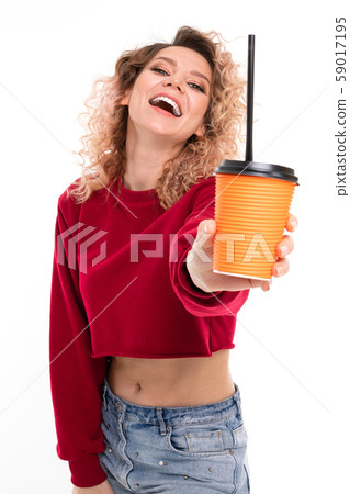 young curly girl with a smile on her face holds a glass of coffee on outstretched hand 59017195