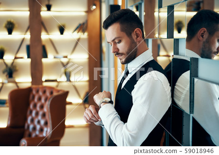 Young business man in dark elegant suit looking at his watch Young business man in dark elegant suit looking at his watch 59018946