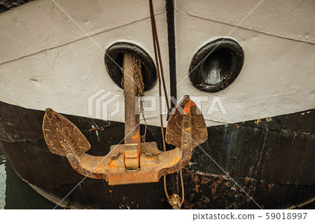 Prow and rusty anchor of a boat moored in port 59018997