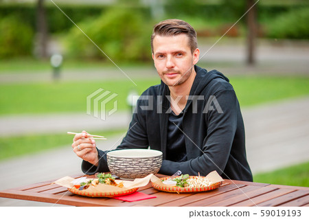 Young man eating take away noodles on the street Young man eating take away noodles on the street 59019193