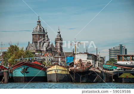 Port with rusty moored ships and church towers in Amsterdam 59019586