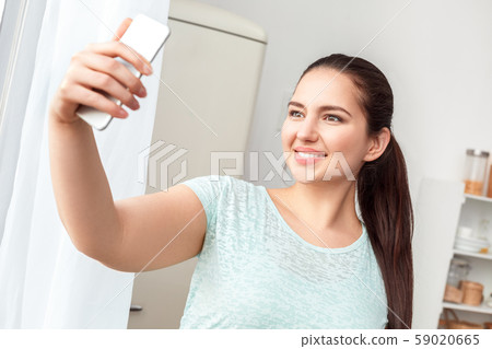 Body Care. Chubby girl standing in kitchen taking selfie on smartphone smiling cheerful to camera Body Care. Chubby girl standing in kitchen taking selfie on smartphone smiling cheerful to camera 59020665