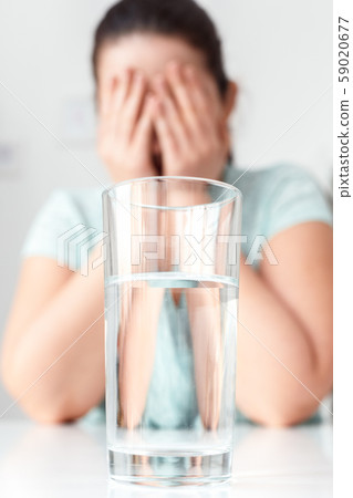Unhappy with Diet. Chubby girl sitting at kitchen table glass of water close-up crying blurred 59020677
