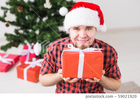 Christmas and holidays concept - Funny man in santa hat holding a gift at home in the living room 59021920