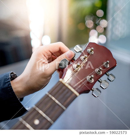 Male hand adjusting pegs on acoustic guitar Male hand adjusting pegs on acoustic guitar 59022573