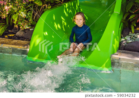 Happy boy on water slide in a swimming pool having fun during summer vacation in a beautiful Happy boy on water slide in a swimming pool having fun during summer vacation in a beautiful 59034232