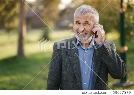Happy elderly man speak with somebody by the phone. Handsome senior man with beautiful beard smile Happy elderly man speak with somebody by the phone. Handsome senior man with beautiful beard smile 59037579