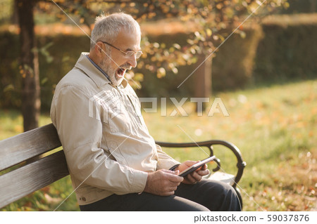 Handsome elderly man sitting on the bench and use tablet for scrolling in internet. Background of 59037876