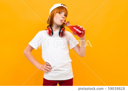 a girl with red beautiful hair stands on a yellow background in a white T-shirt, drinks a red drink 59039828
