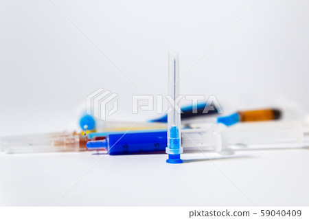 Medical needle on the background of a set of medical syringes with colored liquids inside. Medical needle on the background of a set of medical syringes with colored liquids inside. 59040409