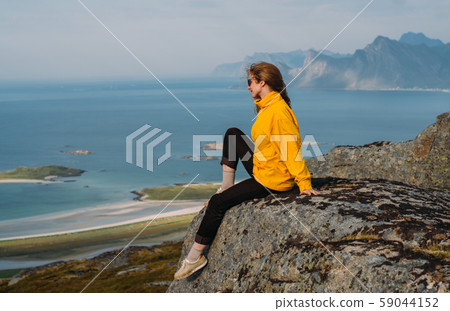 Girl in yellow jacket stitting on stone  59044152
