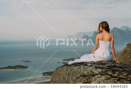 Back of girl in wedding dress sitting on rocks Back of girl in wedding dress sitting on rocks 59044165