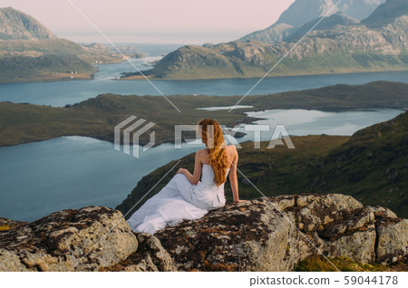 Back of girl in wedding dress sitting on rocks  59044178