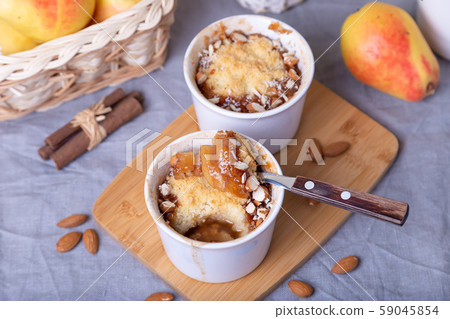Crumble with caramelized pear, cinnamon and almonds in a white ramekin. Close-up. 59045854