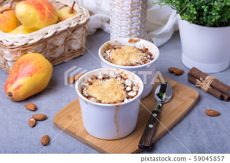 Crumble with caramelized pear, cinnamon and almonds in a white ramekin. Close-up. Crumble with caramelized pear, cinnamon and almonds in a white ramekin. Close-up. 59045857