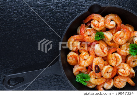 tasty roasted shrimps in a cast iron pan with parsley and garlic, on black background 59047324