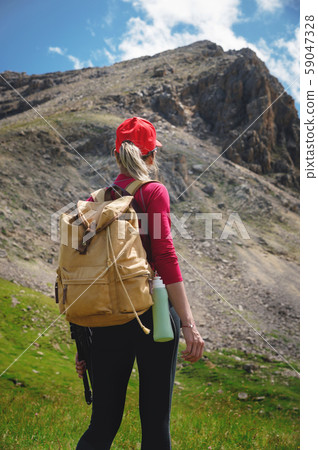 View from the back Girl athlete in a red cap sunglasses and a yellow backpack stands on a green View from the back Girl athlete in a red cap sunglasses and a yellow backpack stands on a green 59047328