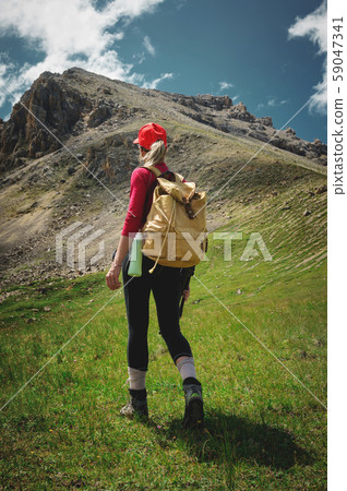 View from the back Girl athlete in a red cap sunglasses and a yellow backpack stands on a green 59047341