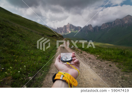 Close-up wide angle male hand with a yellow watch bracelet holds a magnetic navigation compass Close-up wide angle male hand with a yellow watch bracelet holds a magnetic navigation compass 59047419