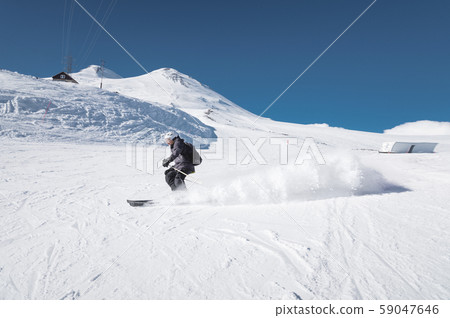 A bearded mature aged male skier in a black ski suit descends along the snowy slope of a ski resort A bearded mature aged male skier in a black ski suit descends along the snowy slope of a ski resort 59047646