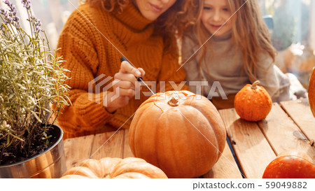 Young adult mother carving pumpkin with her little daughter Young adult mother carving pumpkin with her little daughter 59049882