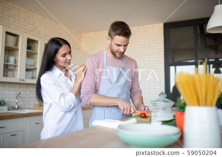 Dark-haired wife hugging husband slicing peppers for salad Dark-haired wife hugging husband slicing peppers for salad 59050204