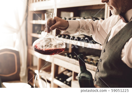 Sommelier Concept. Senior man standing decanter stirring wine in decanter pensive side view close-up 59051225