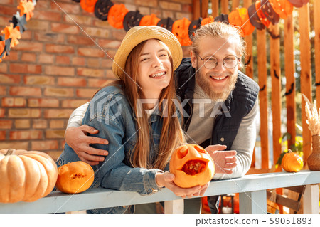 Halloween Preparaton Concept. Young couple leaning on fence decorating house with jack-o'-lantern Halloween Preparaton Concept. Young couple leaning on fence decorating house with jack-o'-lantern 59051893