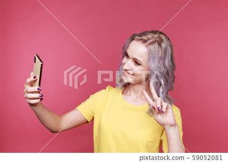 Blond young stylish woman with curly hair showing peace and making photo isolated in the studio. Blond young stylish woman with curly hair showing peace and making photo isolated in the studio. 59052081
