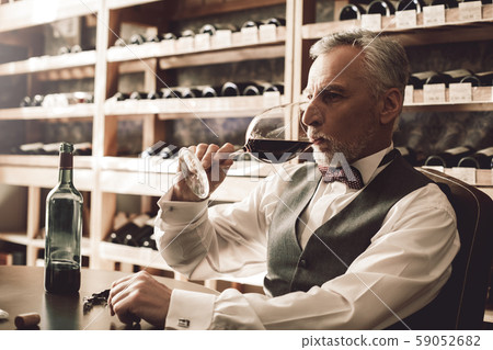 Sommelier Concept. Senior man sitting at table tasting red wine concentrated close-up Sommelier Concept. Senior man sitting at table tasting red wine concentrated close-up 59052682