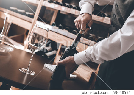 Sommelier Concept. Senior man standing opening wine bottle with corkscrew close-up Sommelier Concept. Senior man standing opening wine bottle with corkscrew close-up 59058535
