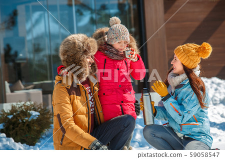 Winter vacation. Family time together outdoors sitting with thermos drinking hot tea laughing happy Winter vacation. Family time together outdoors sitting with thermos drinking hot tea laughing happy 59058547
