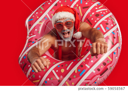 Christmas Freestyle. Young Santa Claus bare muscular upper body in hat and sunglasses standing Christmas Freestyle. Young Santa Claus bare muscular upper body in hat and sunglasses standing 59058567