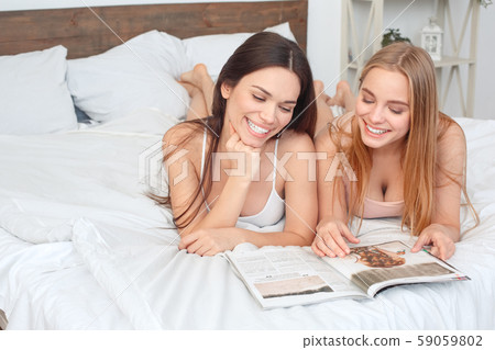Friends together at home lying on bed reading magazine happy Friends together at home lying on bed reading magazine happy 59059802