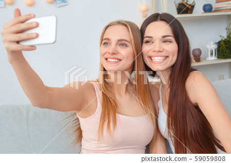 Friends together at home beauty care sitting taking selfie photos on smartphone joyful Friends together at home beauty care sitting taking selfie photos on smartphone joyful 59059808