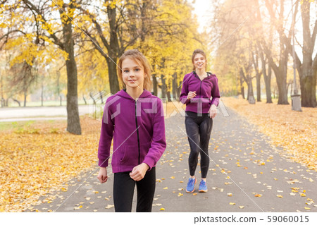 Outdoors leisure. Sisters jogging in the autumn park smiling joyful 59060015