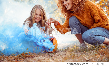 Young adult mother and daughter looking at carved pumpkin with smoke Young adult mother and daughter looking at carved pumpkin with smoke 59061912