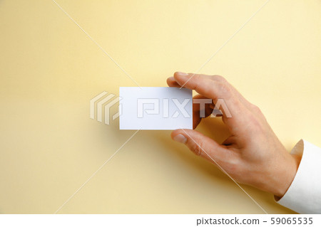 Male hand holding a blank business card on soft yellow background for text or design 59065535