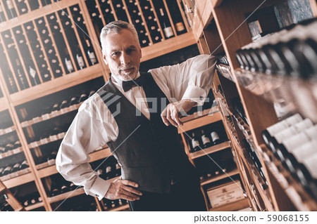 Sommelier Concept. Senior man leaning on wine cabinet looking camera concerned Sommelier Concept. Senior man leaning on wine cabinet looking camera concerned 59068155