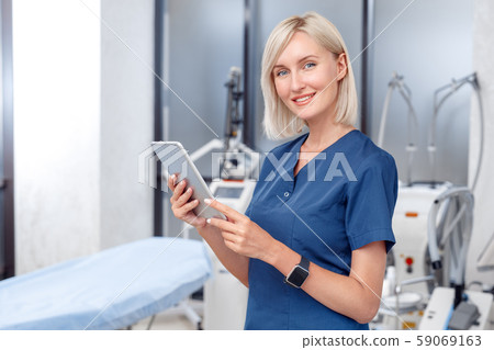 Cosmetology Service. Young doctor standing with digital smiling joyful tablet close-up at beauty Cosmetology Service. Young doctor standing with digital smiling joyful tablet close-up at beauty 59069163