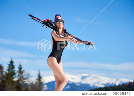 Smilling girl in black swimsuit standing with skis under sun at ski resort Smilling girl in black swimsuit standing with skis under sun at ski resort 59069345