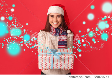 Celebration Concept. Young woman in scarf and santa hat standing isolated on red giving present to 59070734